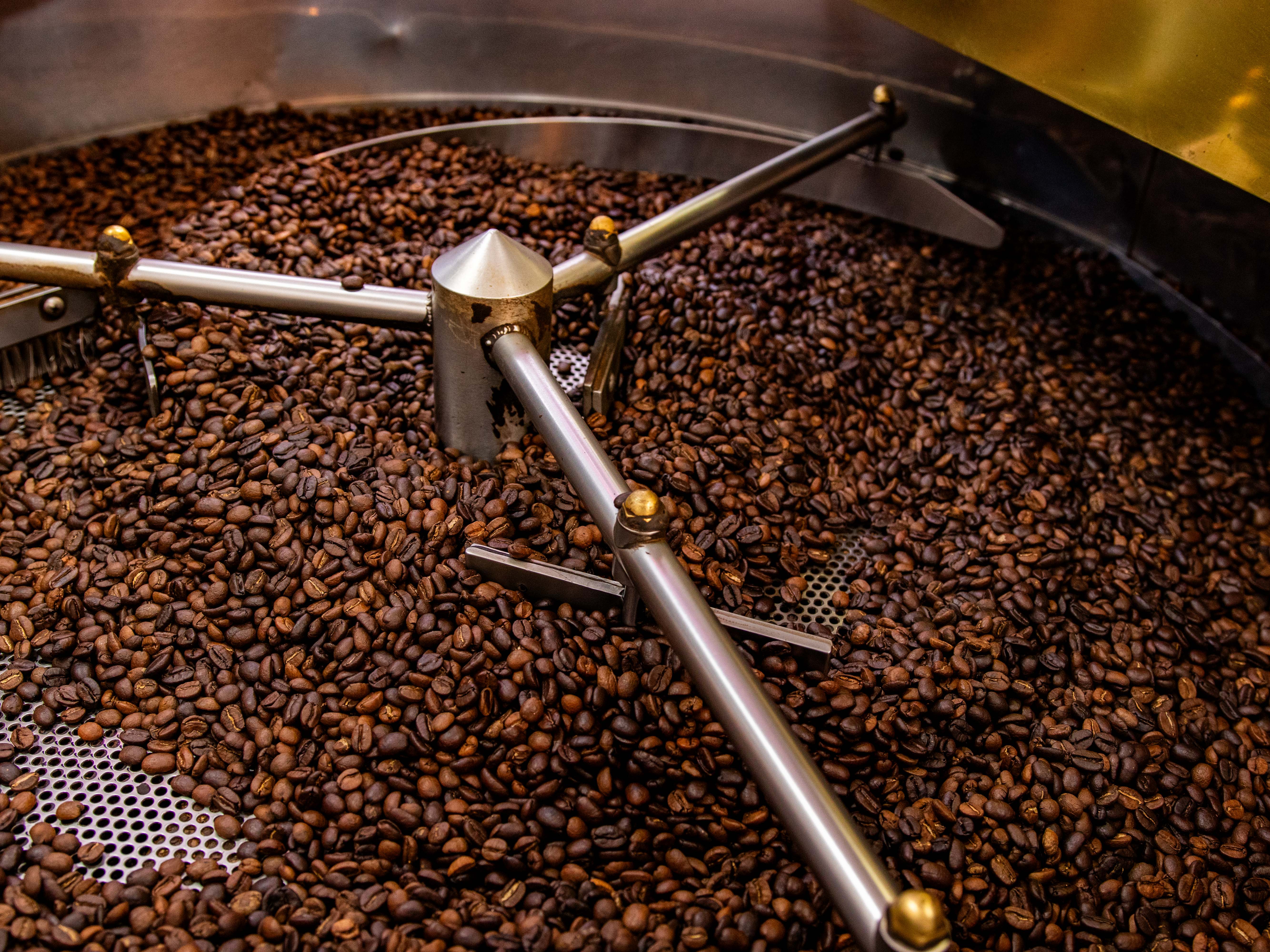 A large industrial coffee roaster, filled with brown coffee beans, dominates the center of the image.