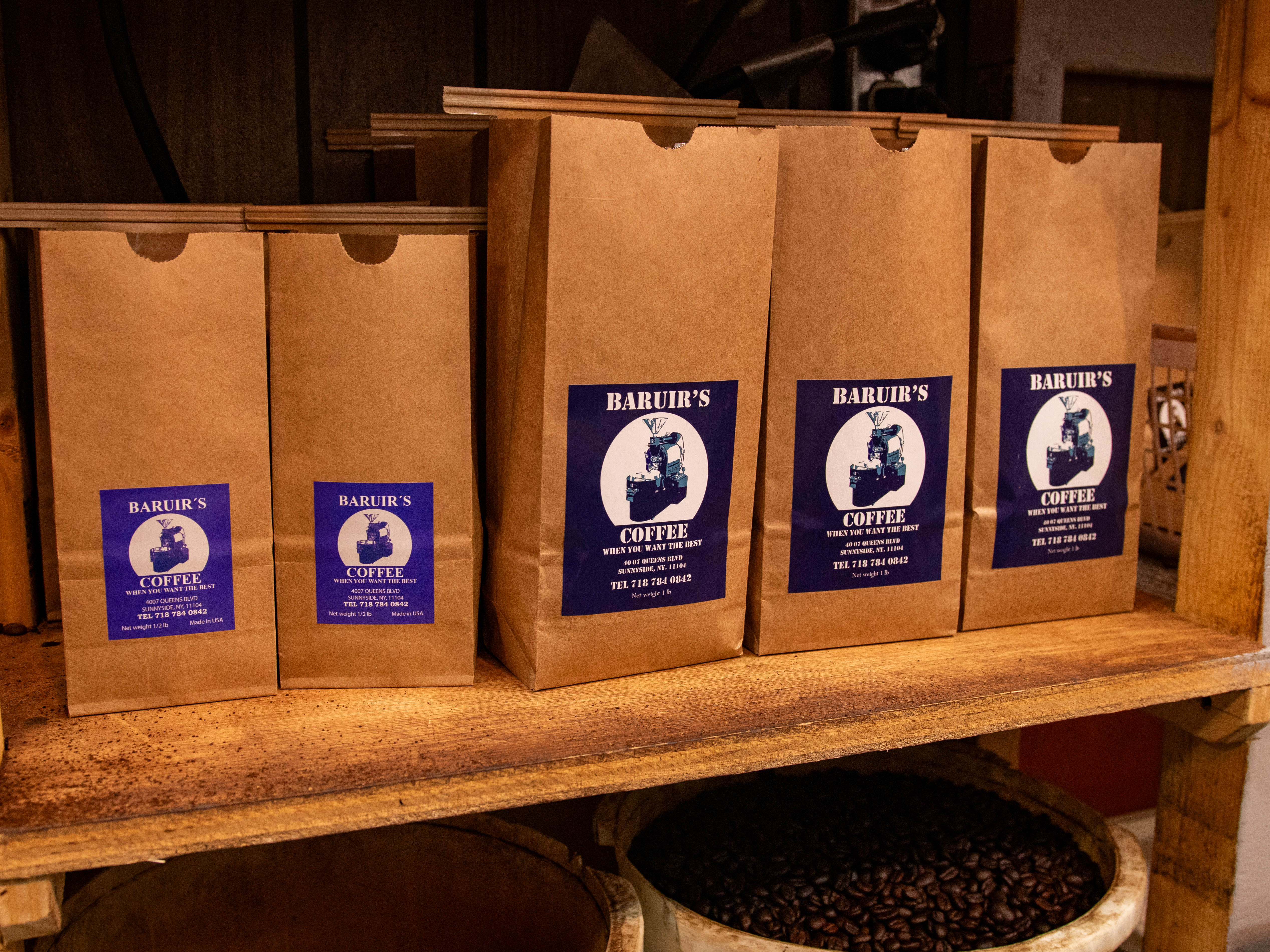 This image depicts a wood shelf holding four brown paper coffee bags and a bucket of raw coffee beans.